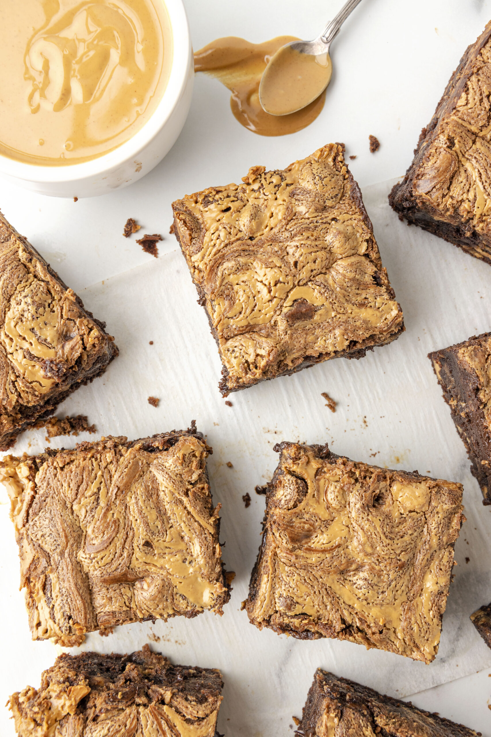 peanut butter swirl brownies laid out on a table with a small dish of creamy peanut butter and a spoon with creamy peanut butter on it resting nearby