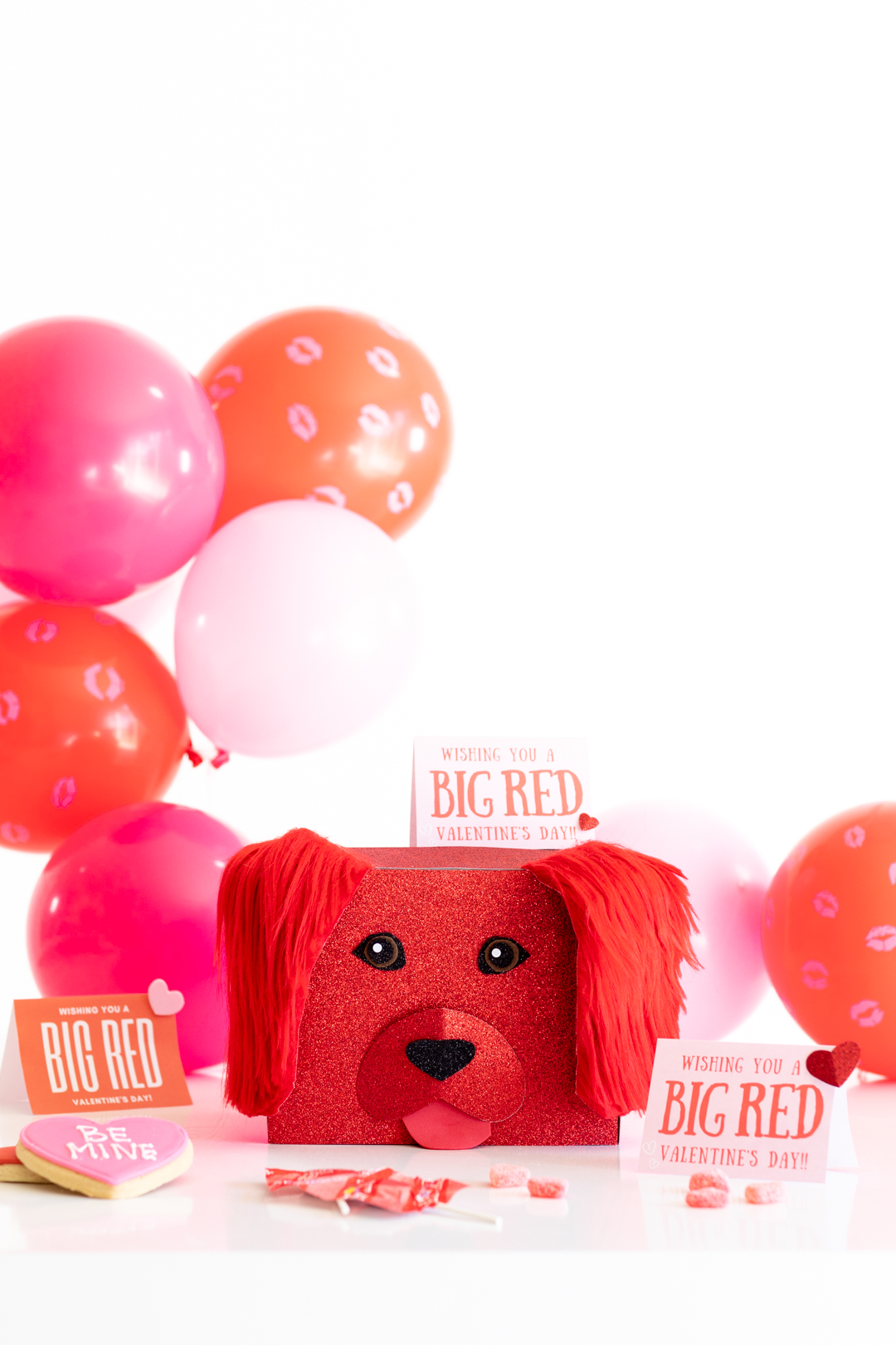 clifford the big red dog movie craft for valentine's day. Card collection box made with red glitter paper and faux red fur. Pink and red balloons in the background and valentine's day cards scattered around the box.