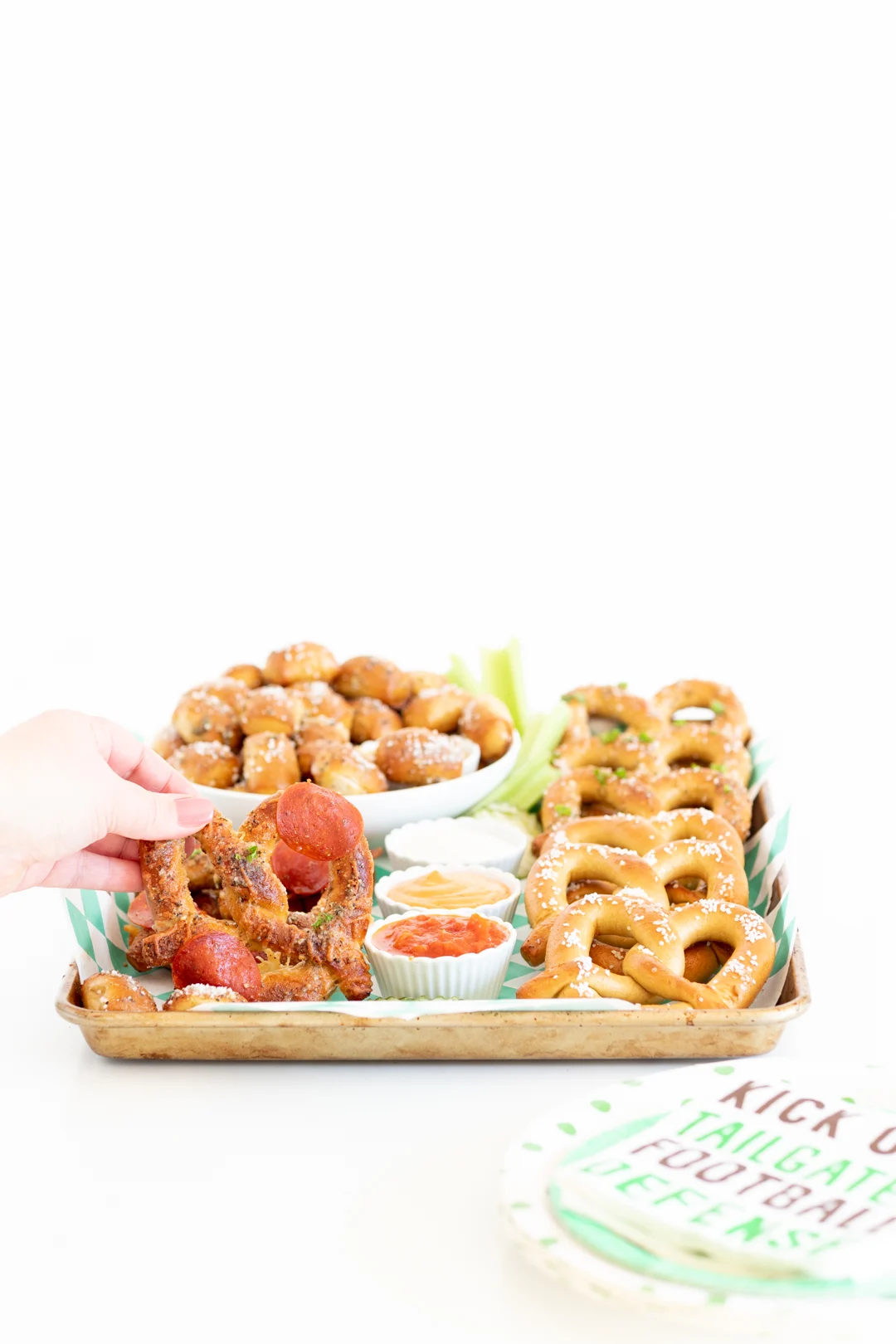 woman about to pick up a pizza soft pretzel off of a game day themed soft pretzel snacking board with a variety of pretzel flavors and dipping sauces