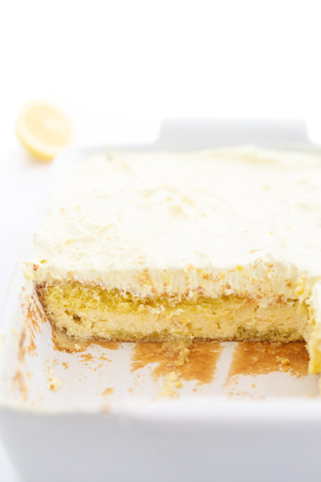 layered lemon cake in a baking dish. bottom ricotta cake layer, middle lemon cake mix layer and top layer lemon pudding frosting on top