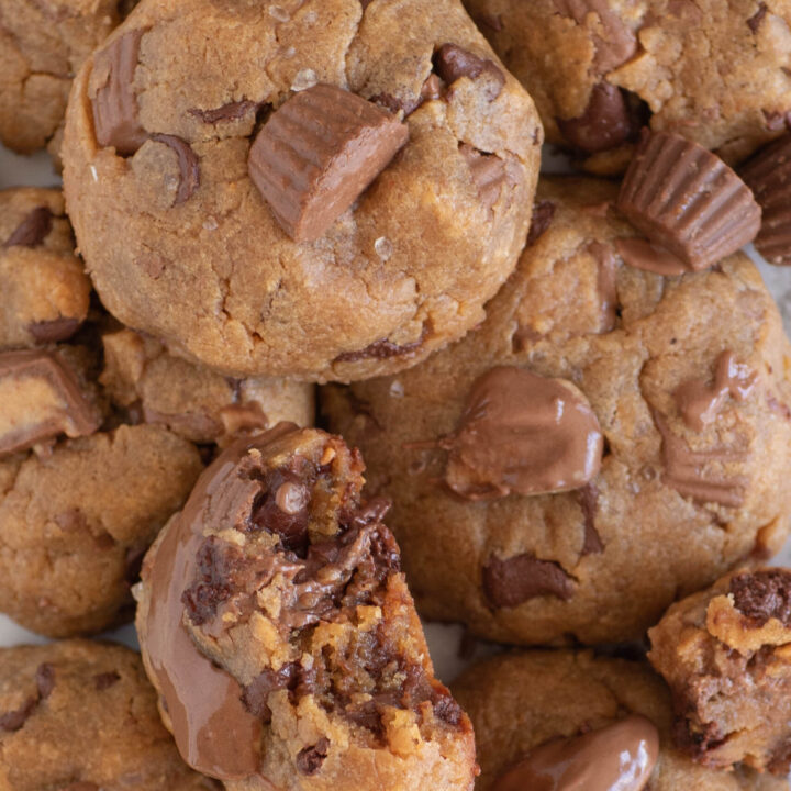 gooey peanut butter cup cookies up close. one cookie with a bite taken out of it revealing lots of melty chocolate chips inside