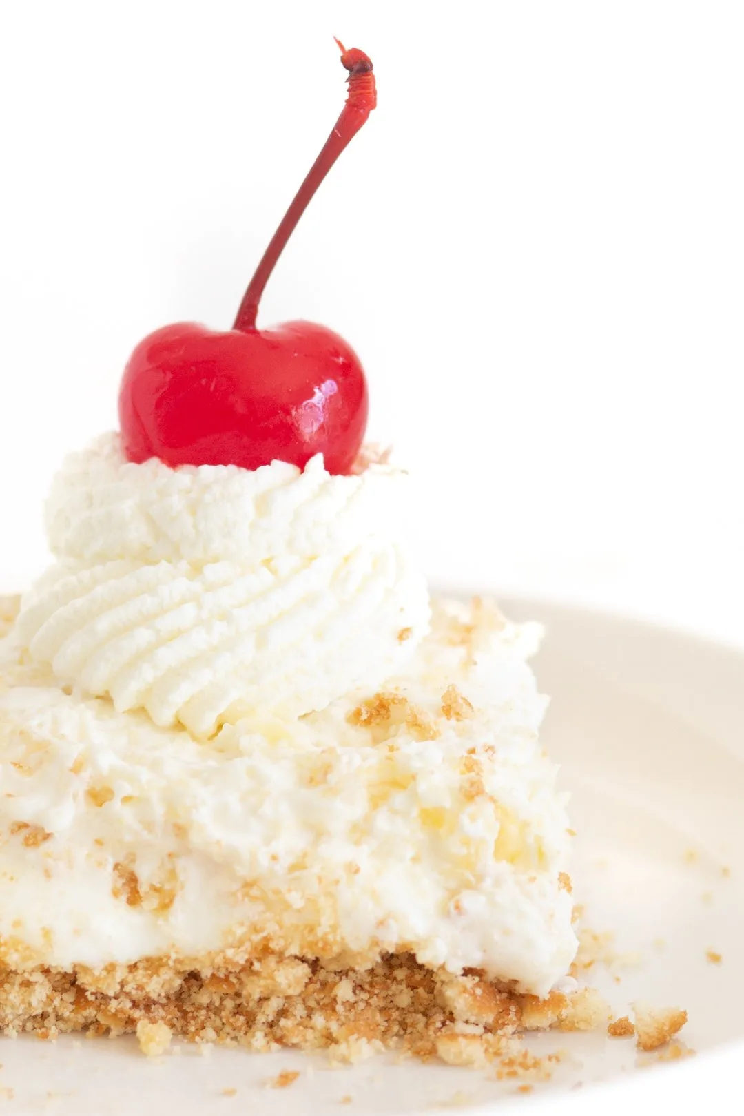 piece of pineapple cream dessert up close. topped with double layer of whipped cream an a maraschino cherry