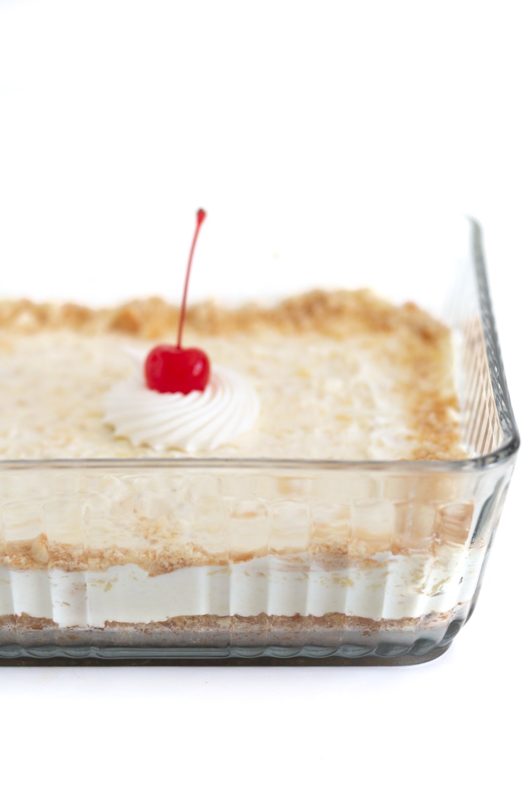 layered pineapple dessert in a glass baking dish. topped with pretty dollop of whipped cream and a cherry