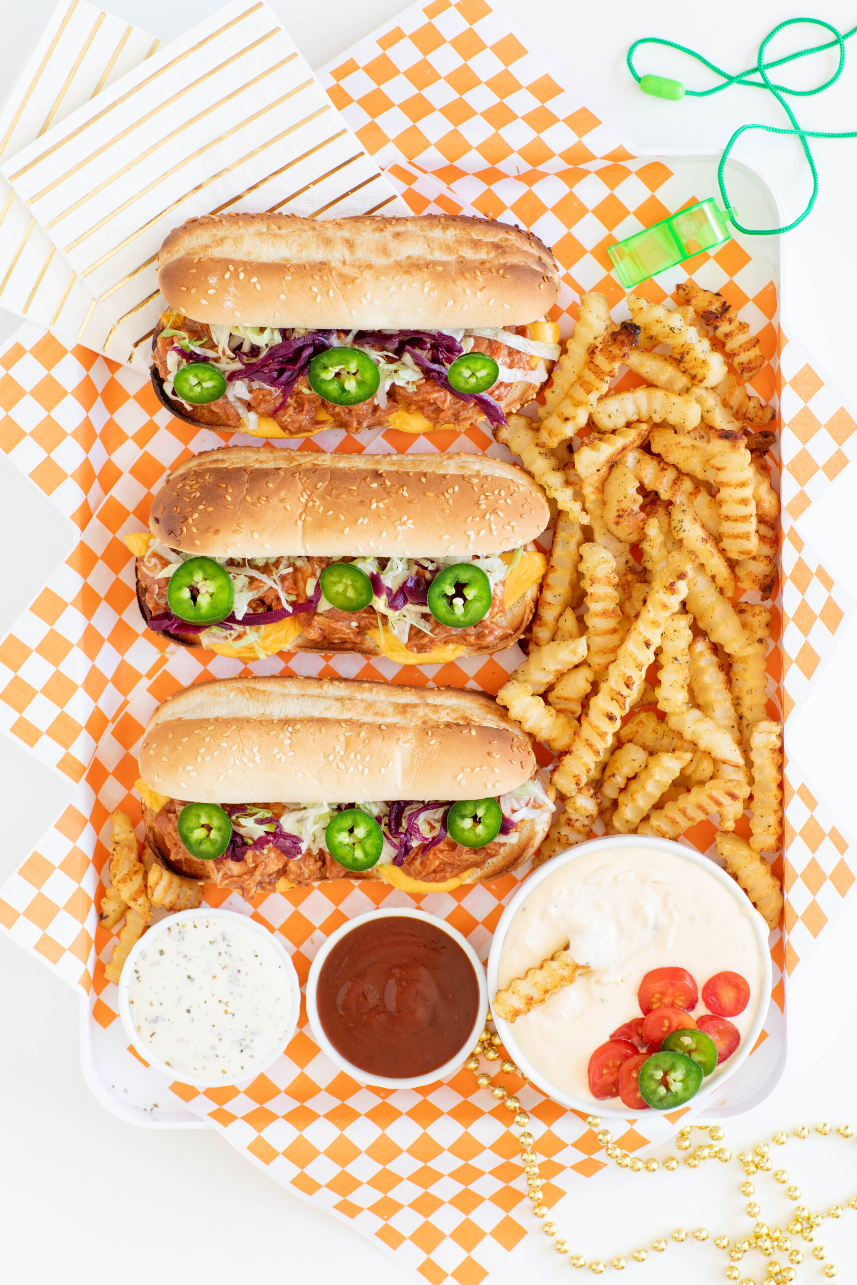 basketball sandwich platter with long pulled chicken sandwiches served in sesame seed buns and topped with jalapeño slices, picked cabbage, shredded lettuce. crinkle fries.