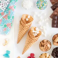 dessert tray to make campfire cones with waffle ice cream cones, mini marshmallows, mini cookies, chocolate bars, sprinkles, graham cereal and more fillings.