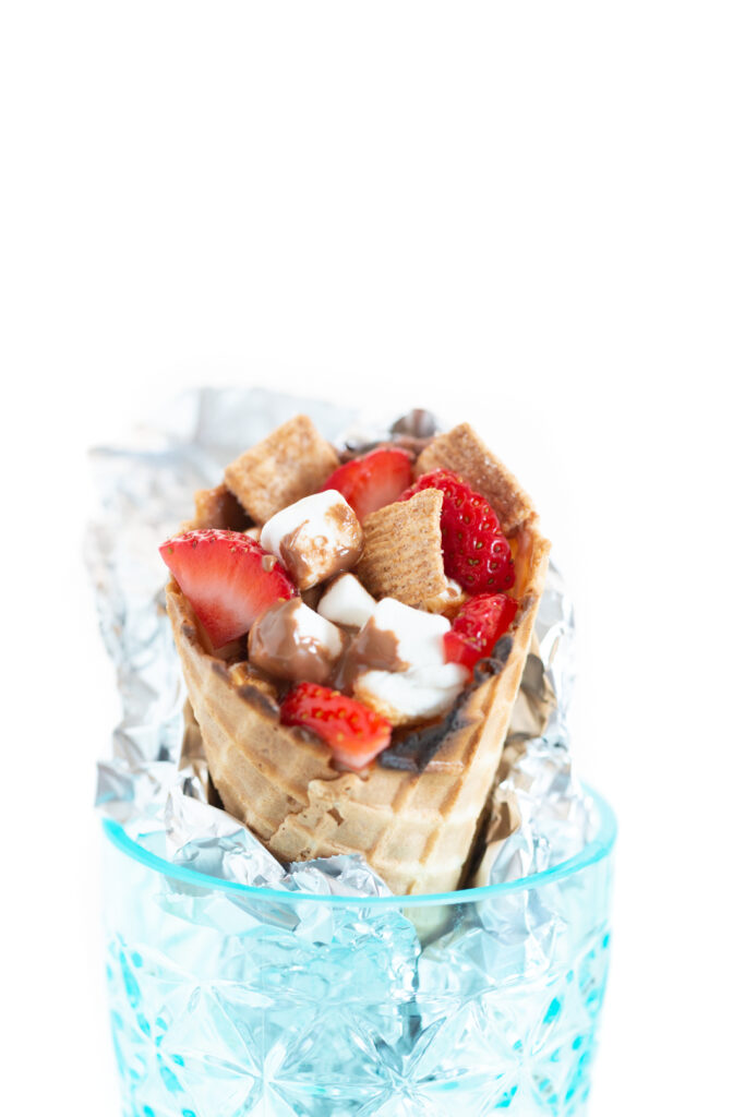up close view of a campfire cone filled with mini marshmallows, strawberry slices, graham cereal and melted chocolate
