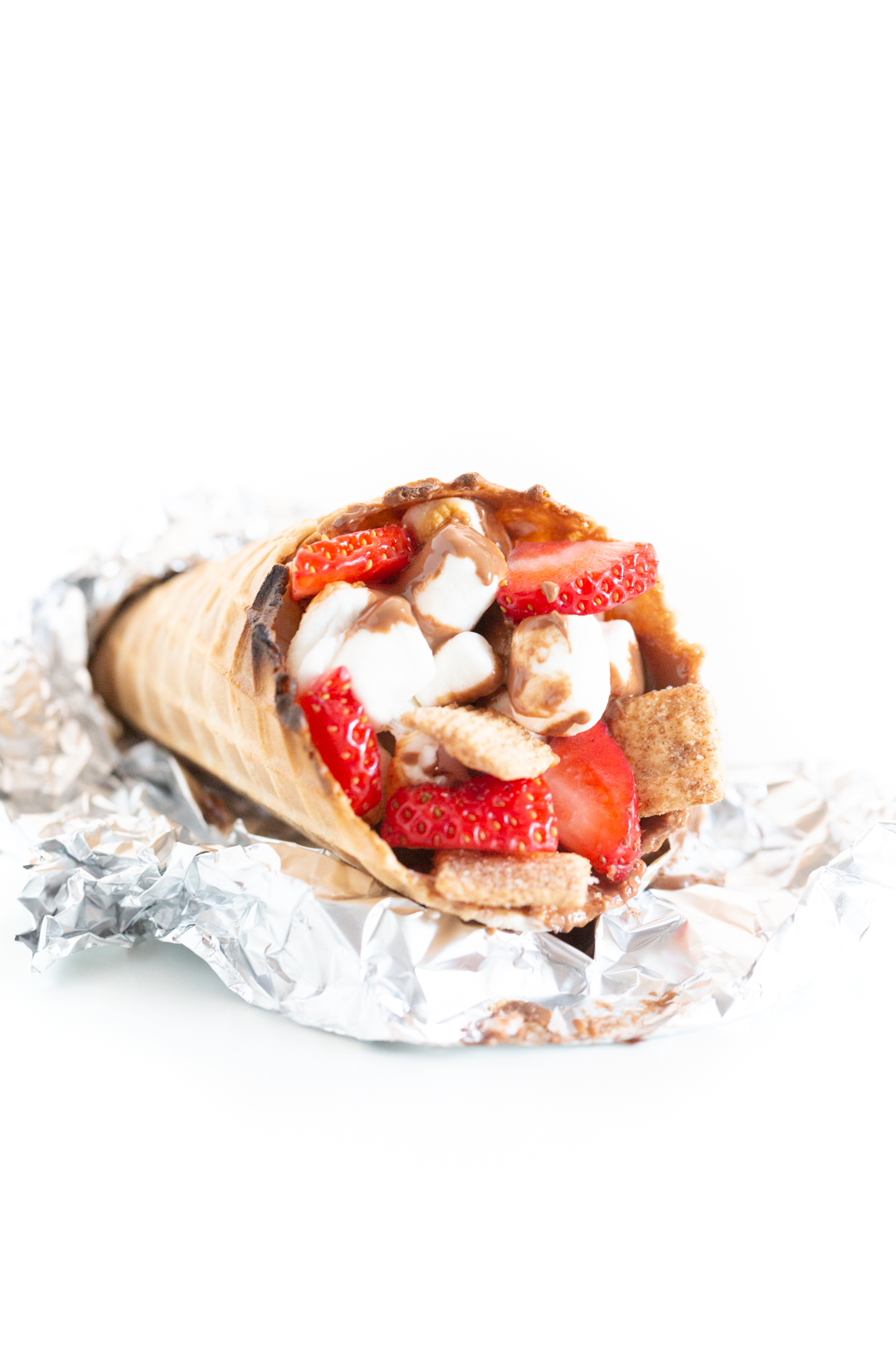 campfire cone laying on foil on a table to reveal the melted chocolate and marshmallow filling inside.