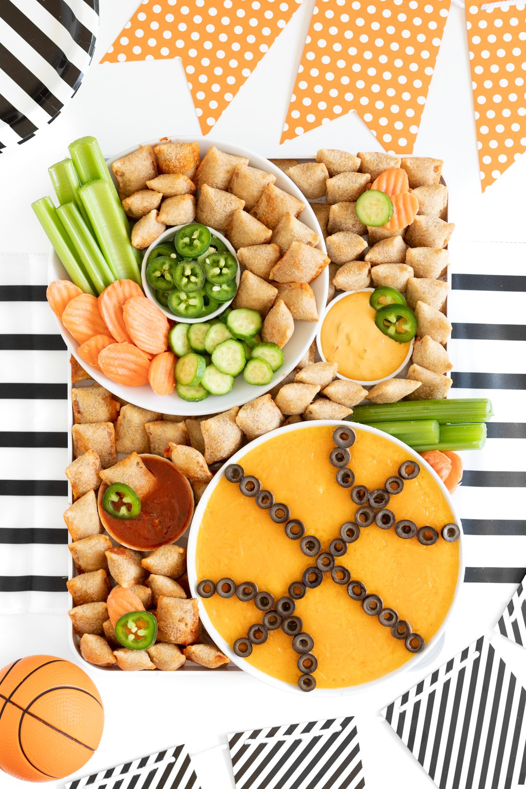 overhead photo of a basketball charcuterie board with basketball shaped dip bowl, vegetables and totinos pizza rolls