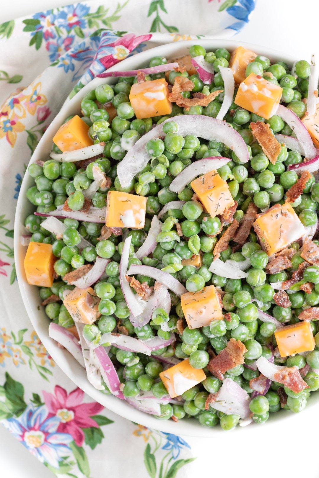 up close view of pea salad with creamy dressing, cheddar cheese chunks, onion slivers and chopped bacon