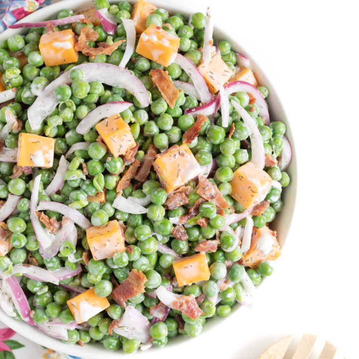 serving dish filled with pea salad with cheese chunks, slivered onions and bacon,