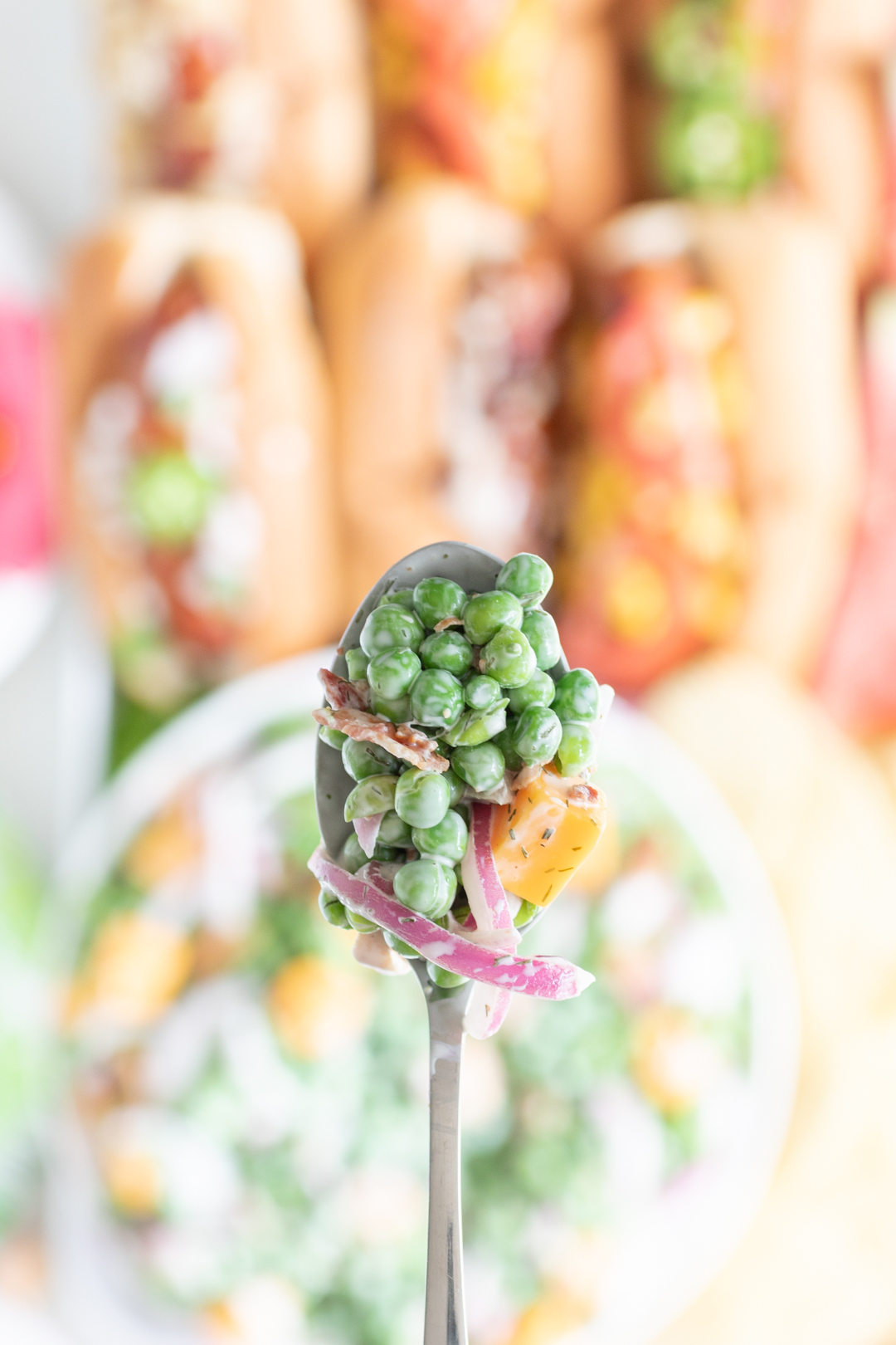 up close view of spoonful of classic summer pea salad with cheese chunk, slivered onions and bacon bits.