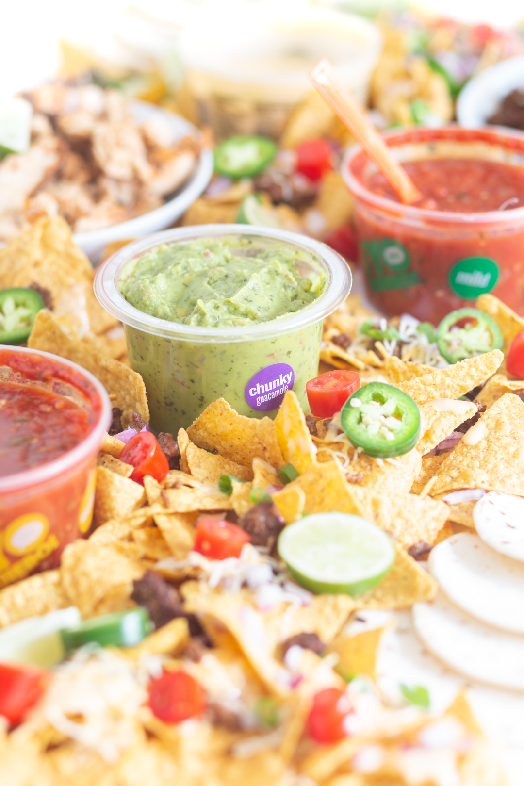 angled view of table nachos.  various bowls of salsa and guacamole set inside of a lot of nachos with toppings.
