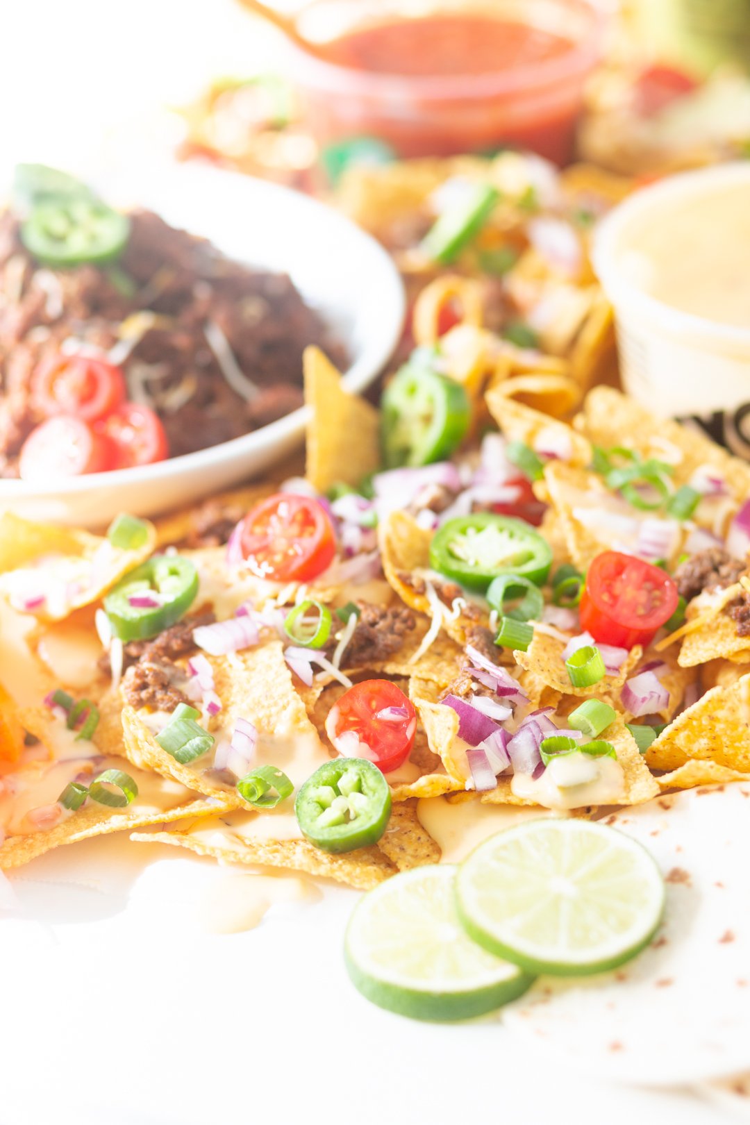 close view of table nachos with traditional toppings and bowl of ground beef.a