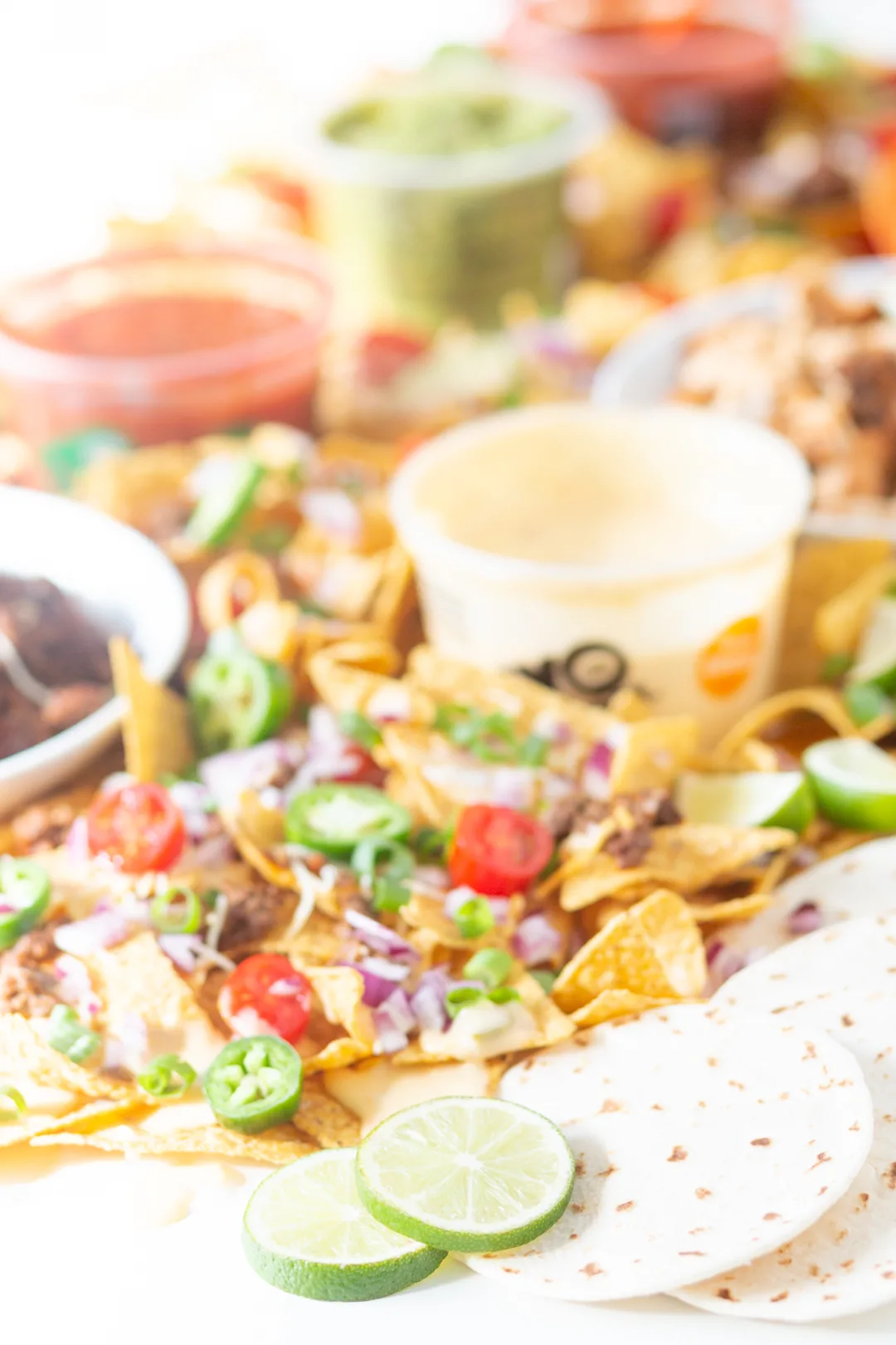 up close view of table nachos. tortilla chips loaded with fresh toppings. sliced grape tomatoes, jalapeño slices, scallions, cheese.
