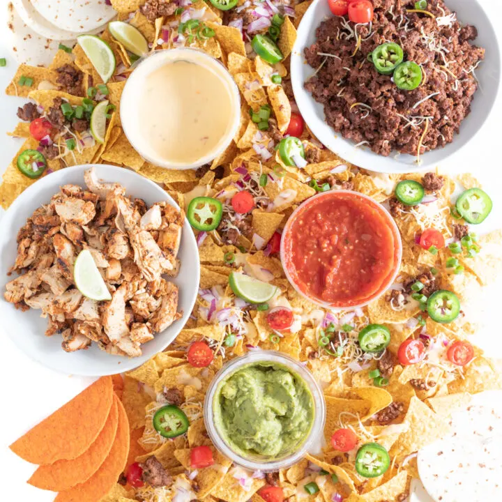 Table Nachos for parties. Huge spread of tortilla chips and nacho toppings spread out over a table. Nacho cheese, salsa, guacamole, ground beef