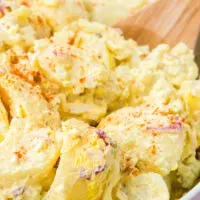 up close angled down view of a bowl of potato salad with a spoon, topped with paprika garnish