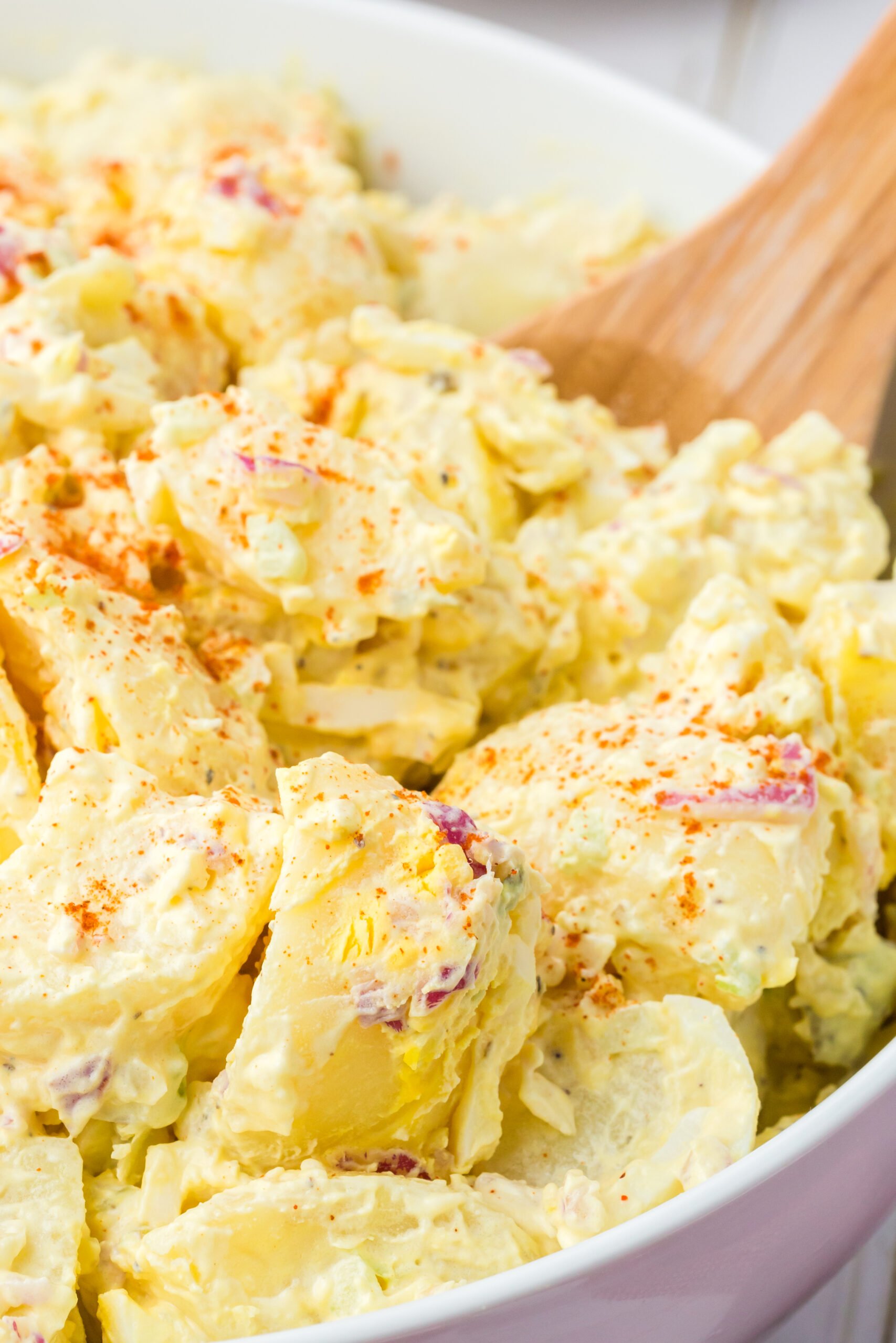 up close angled down view of a bowl of potato salad with a spoon, topped with paprika garnish
