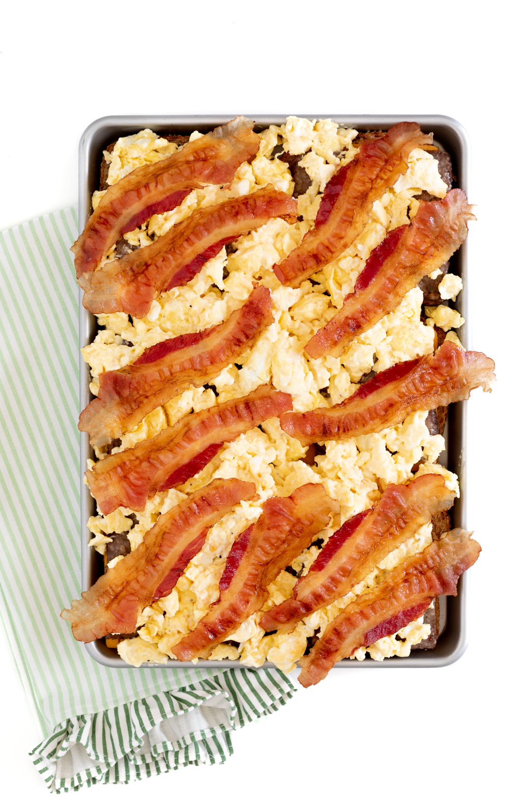 bacon lined on top of scrambled eggs in a baking sheet to prepare sliders