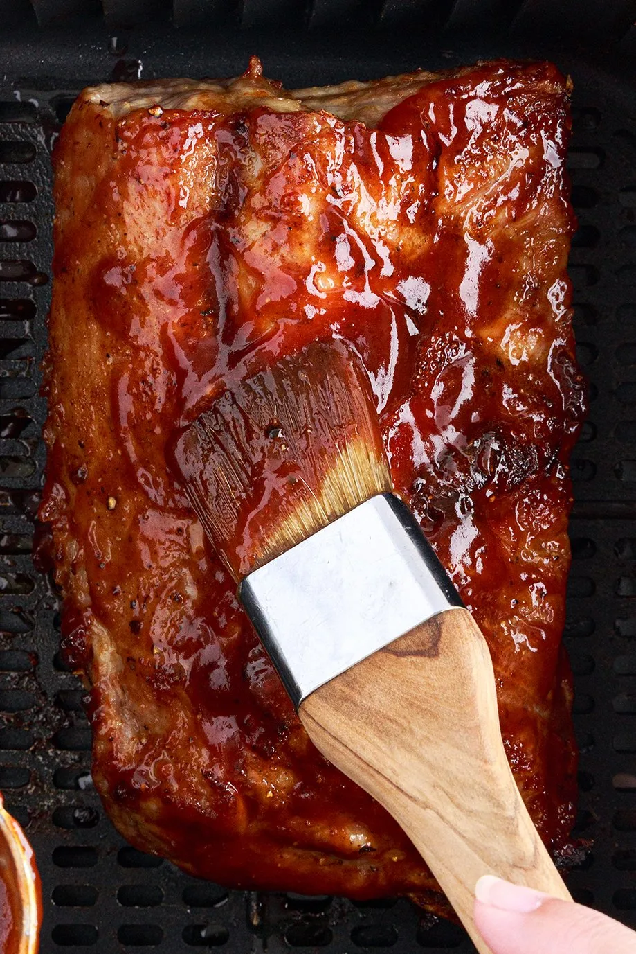 using a food brush to slather on bbq sauce onto air fried ribs