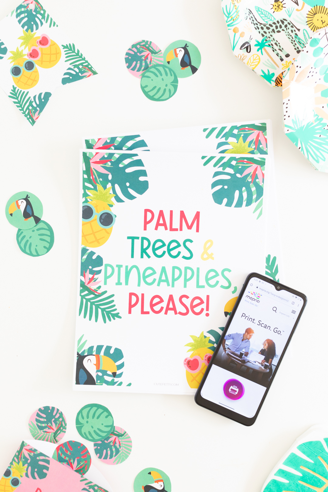 overhead photo of tropical party printables and a cell phone demonstrating how to use an app to print