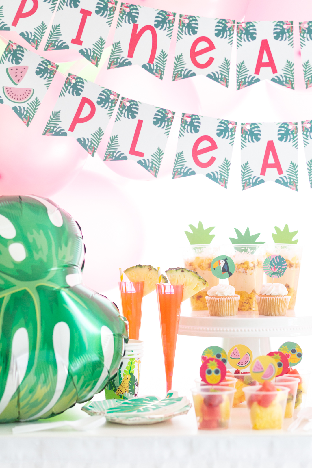 tropical party table with pink balloons and various tropical treats