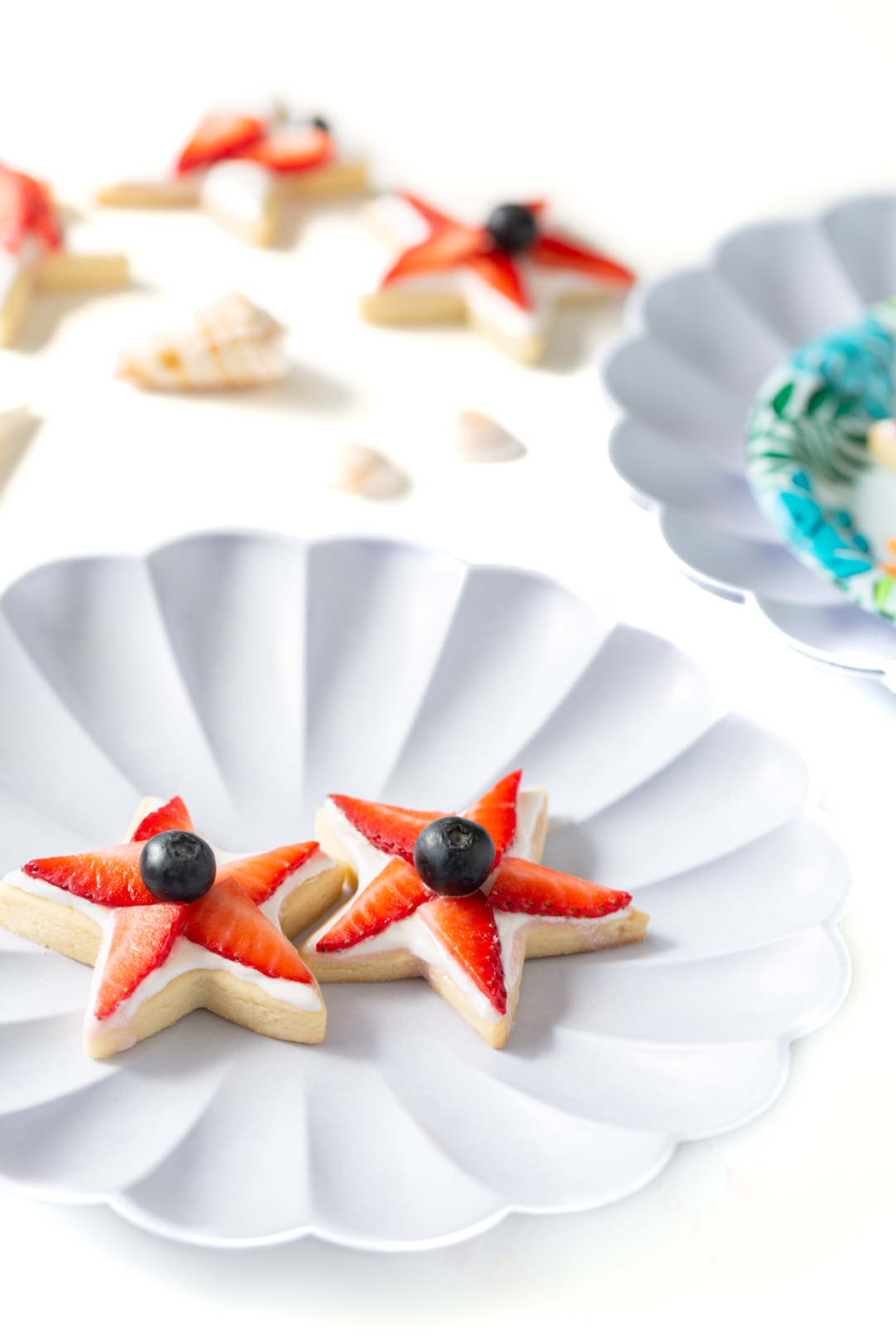 two star shaped cookies with strawberry pieces and blueberries on top resting on a shell inspired plate
