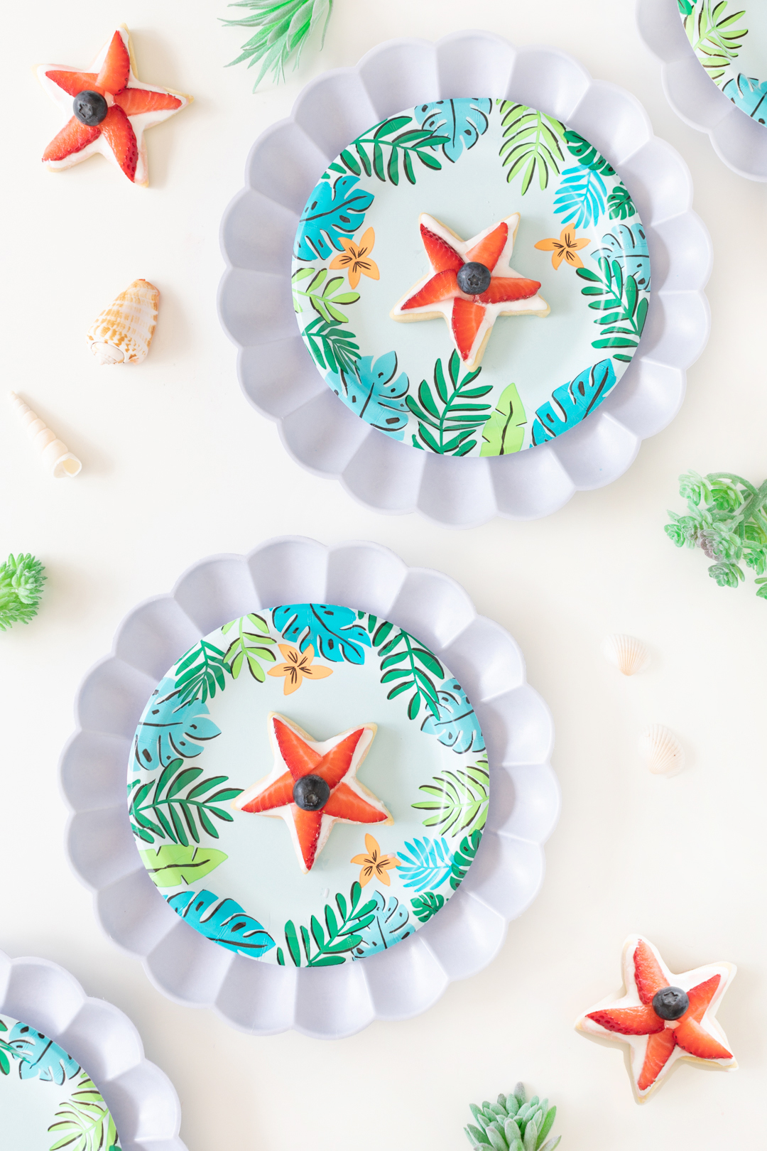 strawberry and blueberry star-shaped sugar cookies set out on cute tropical paper plates with a sea shell charger.