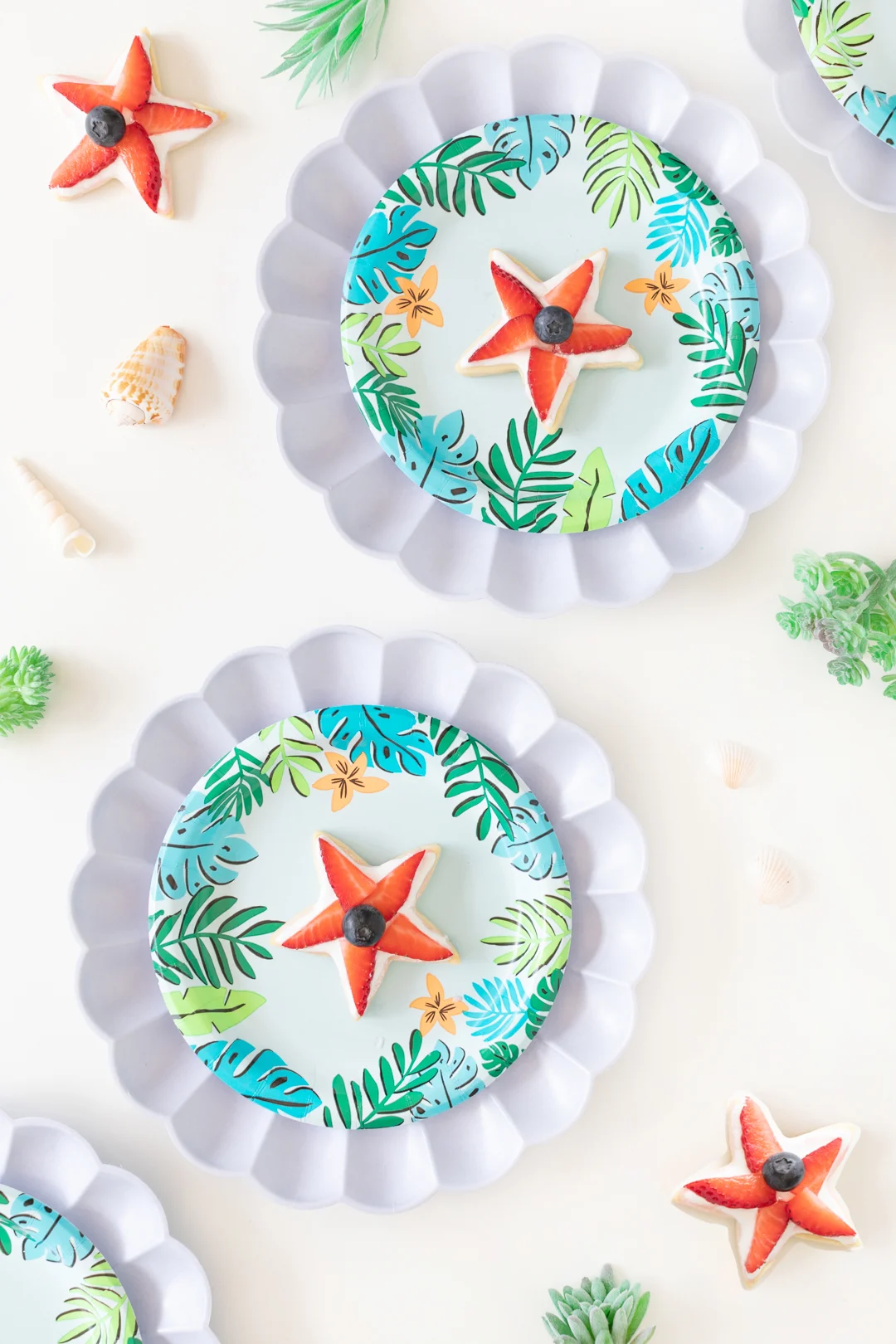 strawberry and blueberry star-shaped sugar cookies set out on cute tropical paper plates with a sea shell charger.