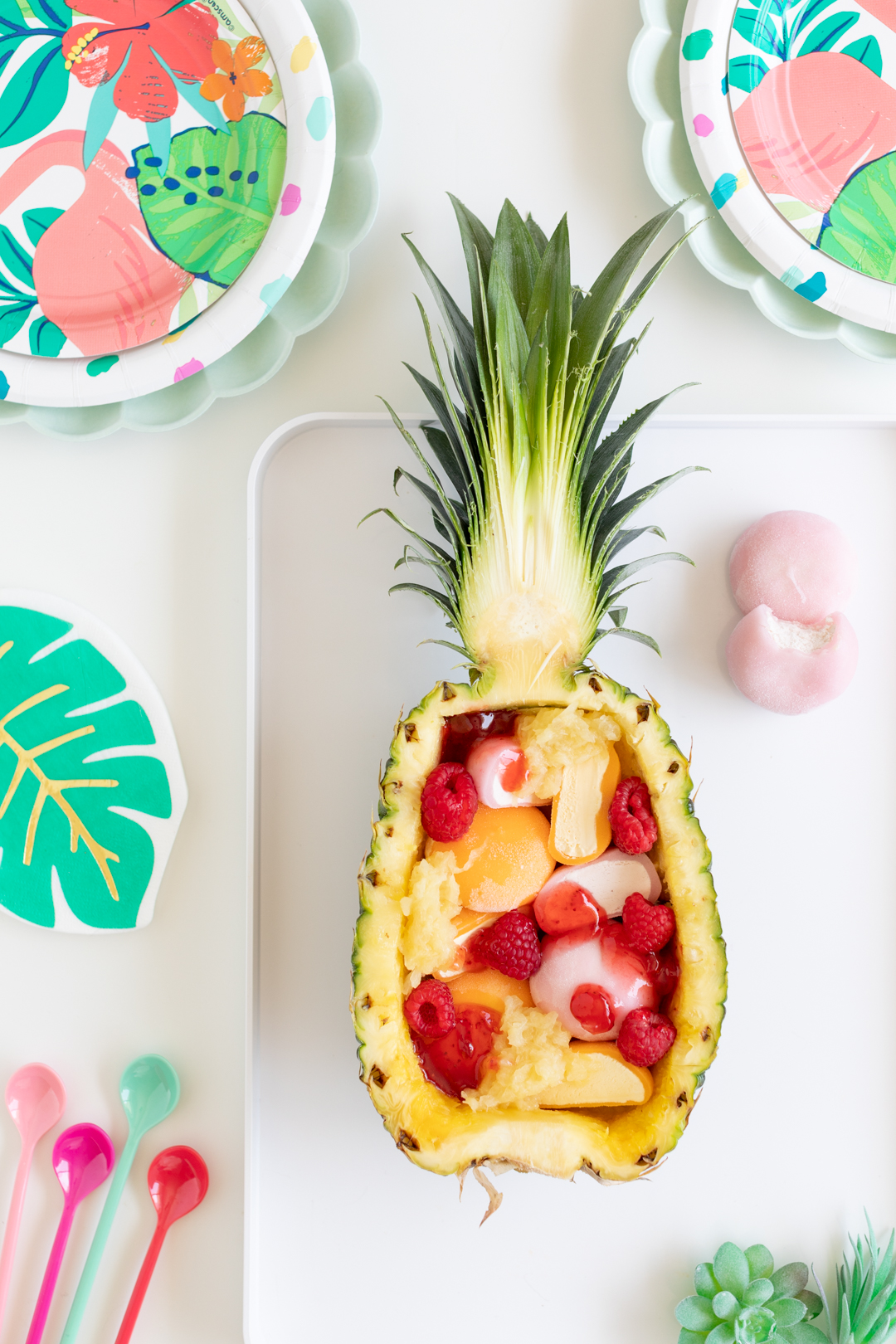 fresh fruits and fruit sauces being added to mochi sundae being made in a halved pineapple