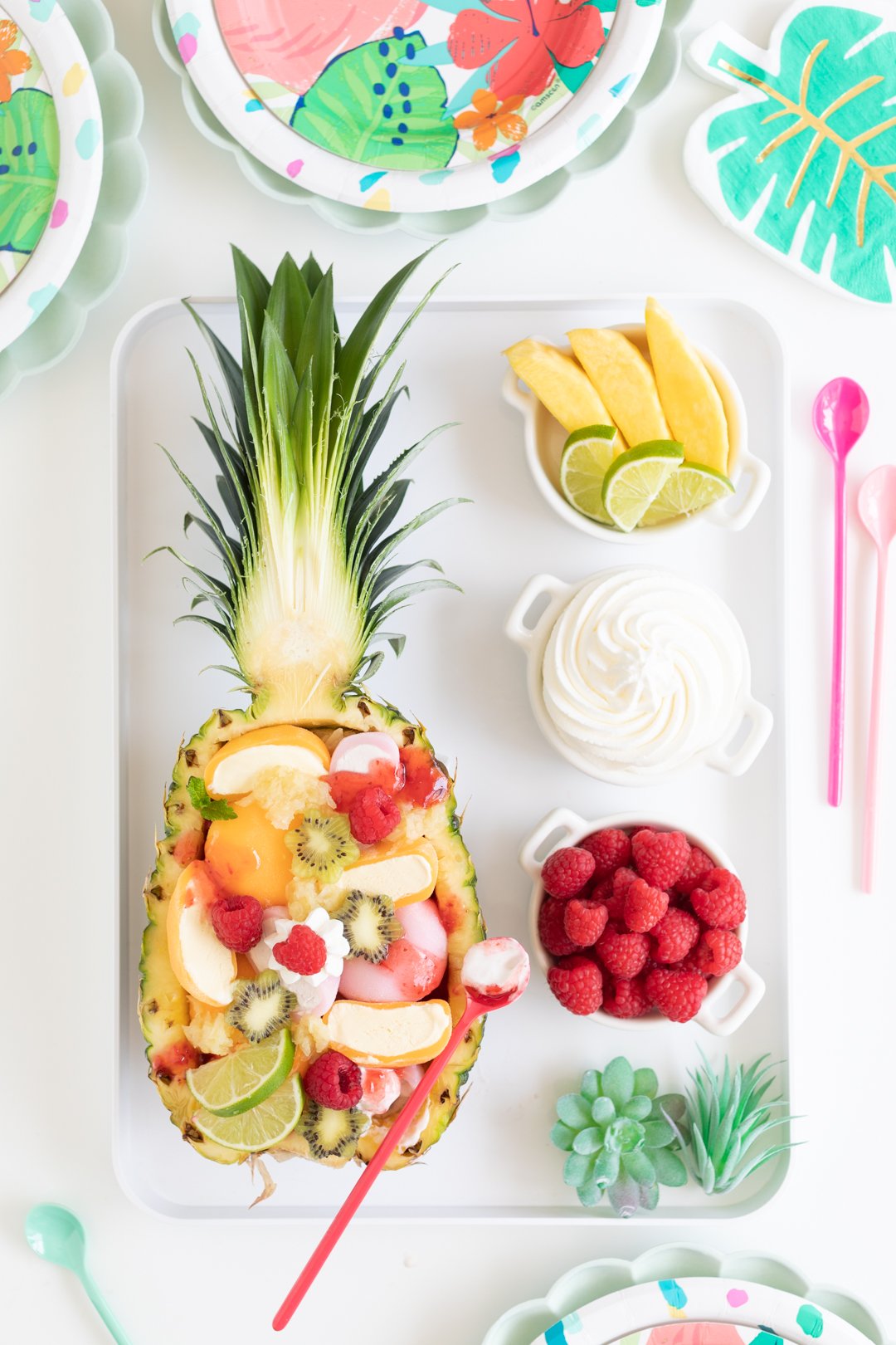 pineapple sundae being served on a white tray with fruit and whipped cream toppings on the side