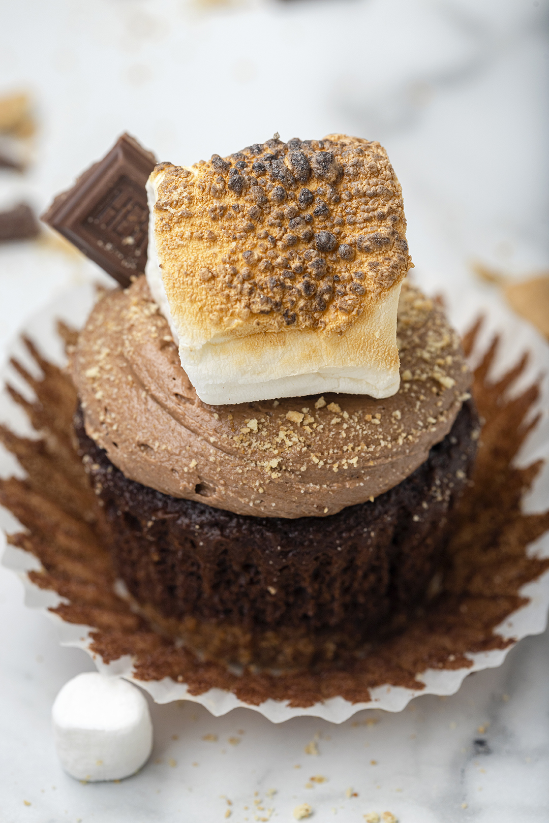 slightly angled shot of s'mores cupcake with chocolate base, chocolate frosting with toasted square marshmallow and Hershey's chocolate