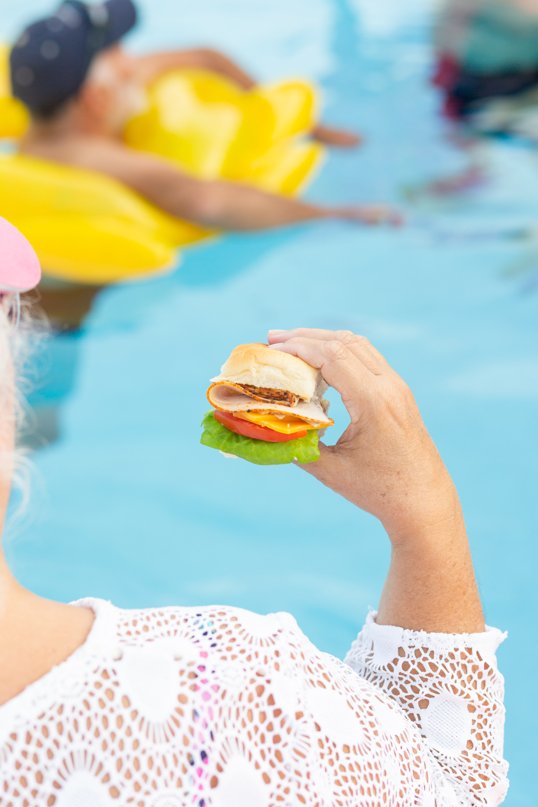 woman holding a slider sandwich while sitting at the pool's edge