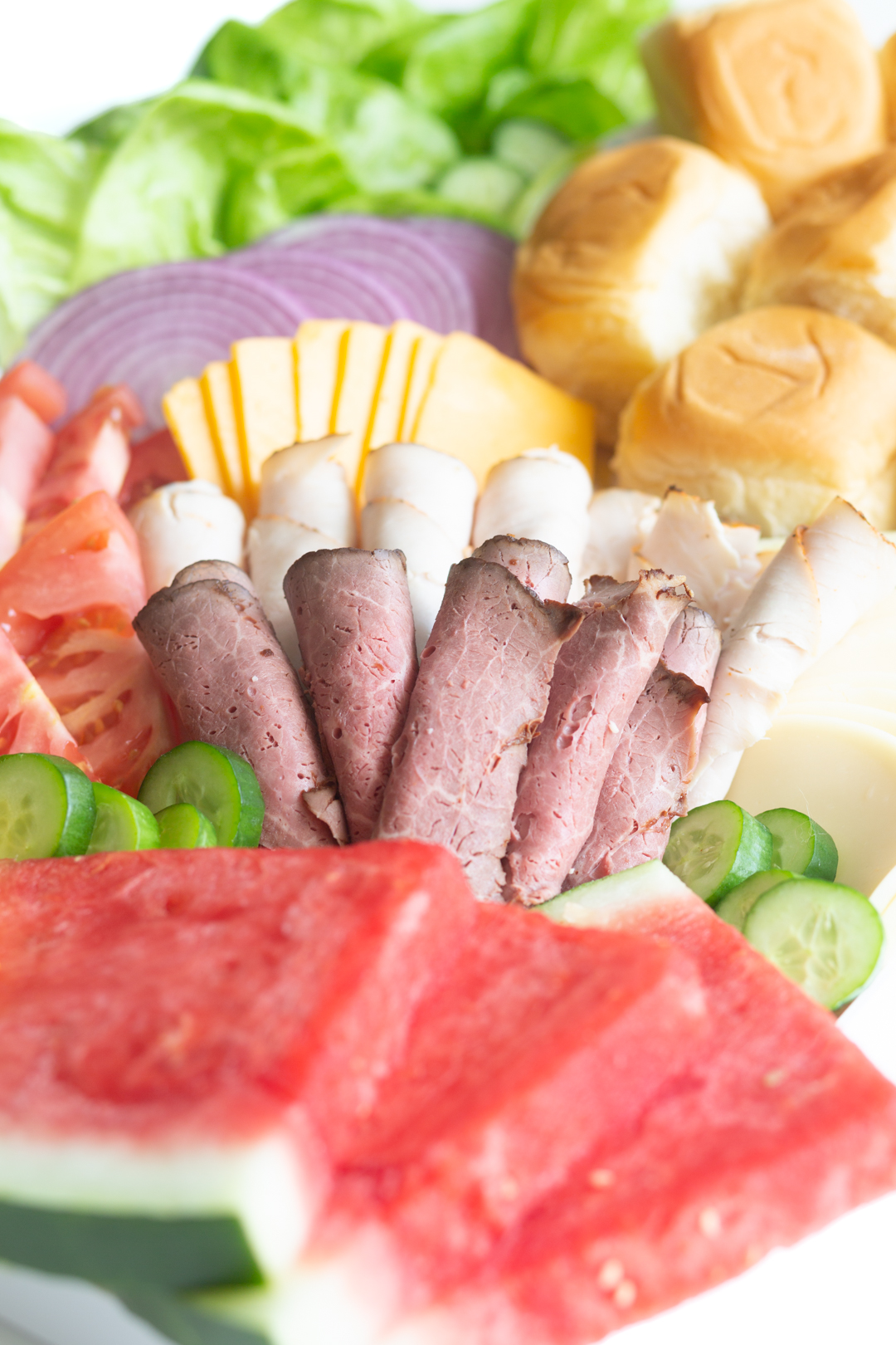 up close angled down photo of slider charcuterie board with rolled lunch meats and sliced fruits and vegetables