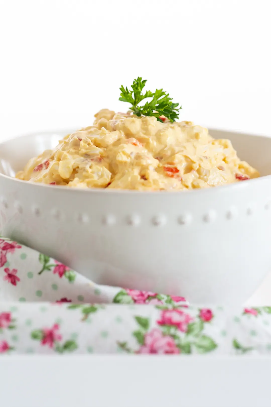 up close view of white bowl filled with egg salad and topped with curly parsley.