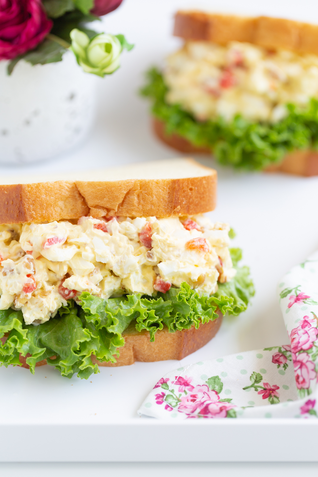 egg salad stuffed into white sliced bread and lined with green leaf lettuce
