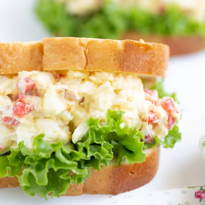 tall stuffed egg salad sandwich with pimientos on a bed of lettuce and white sliced bread