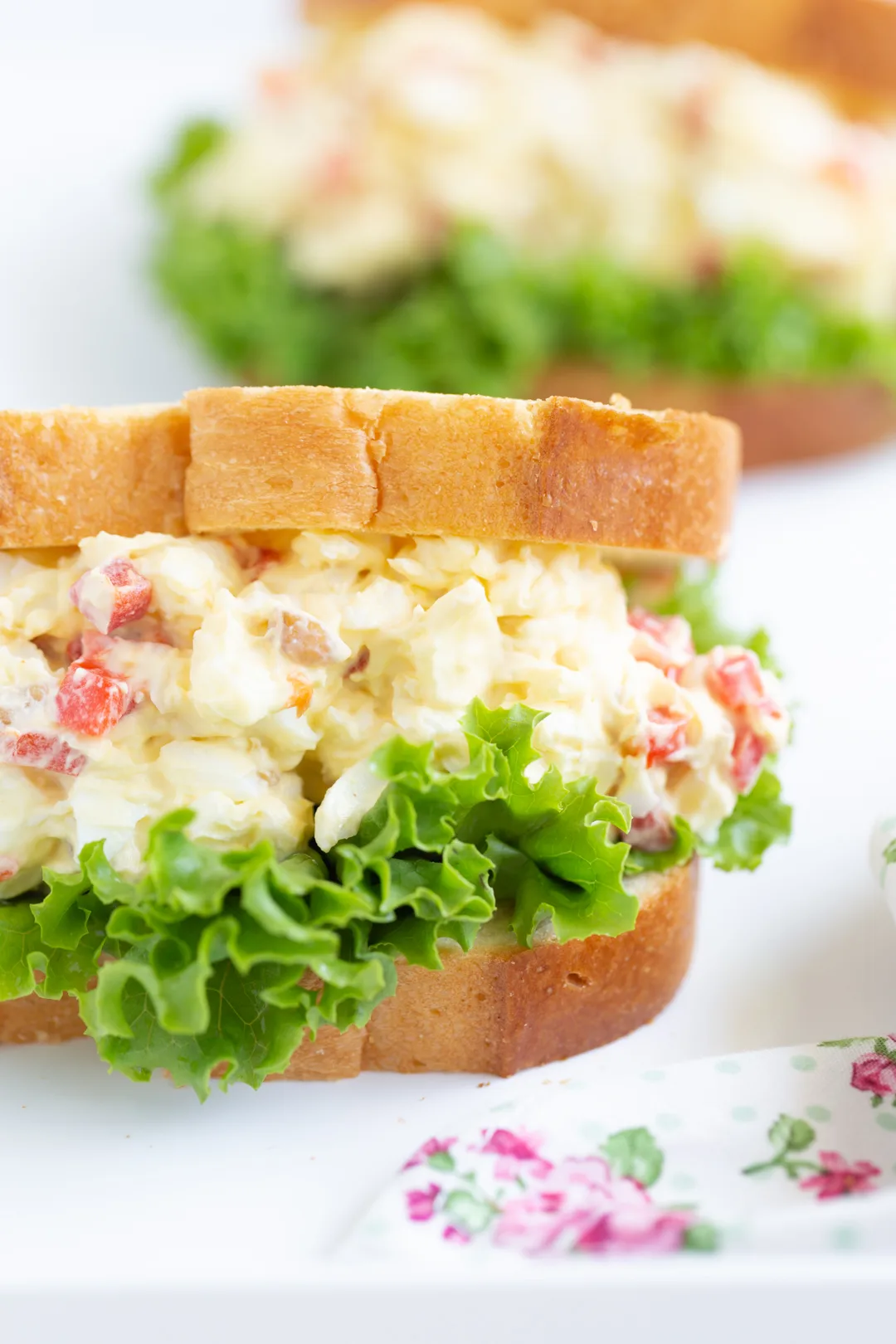 tall stuffed egg salad sandwich with pimientos on a bed of lettuce and white sliced bread