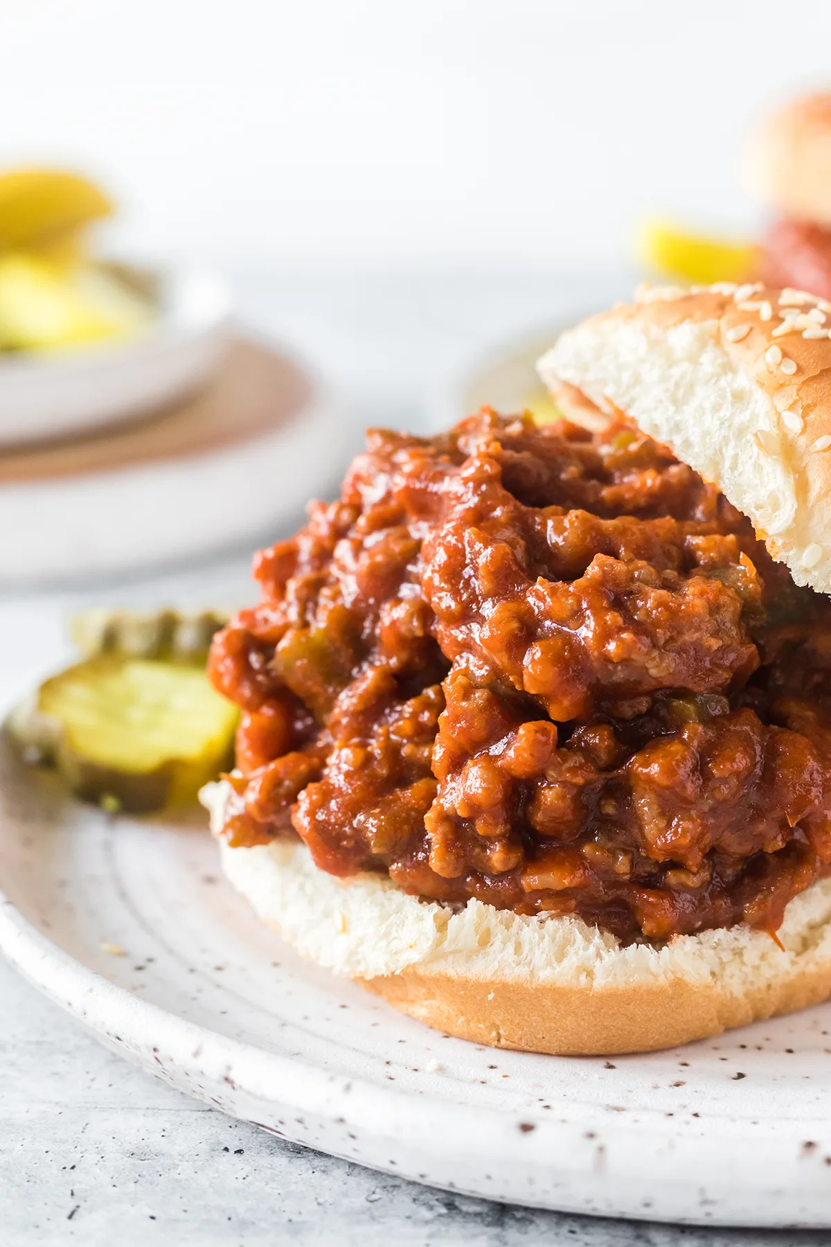 open faced sloppy joe sandwich on a small white plate served with pickle slices