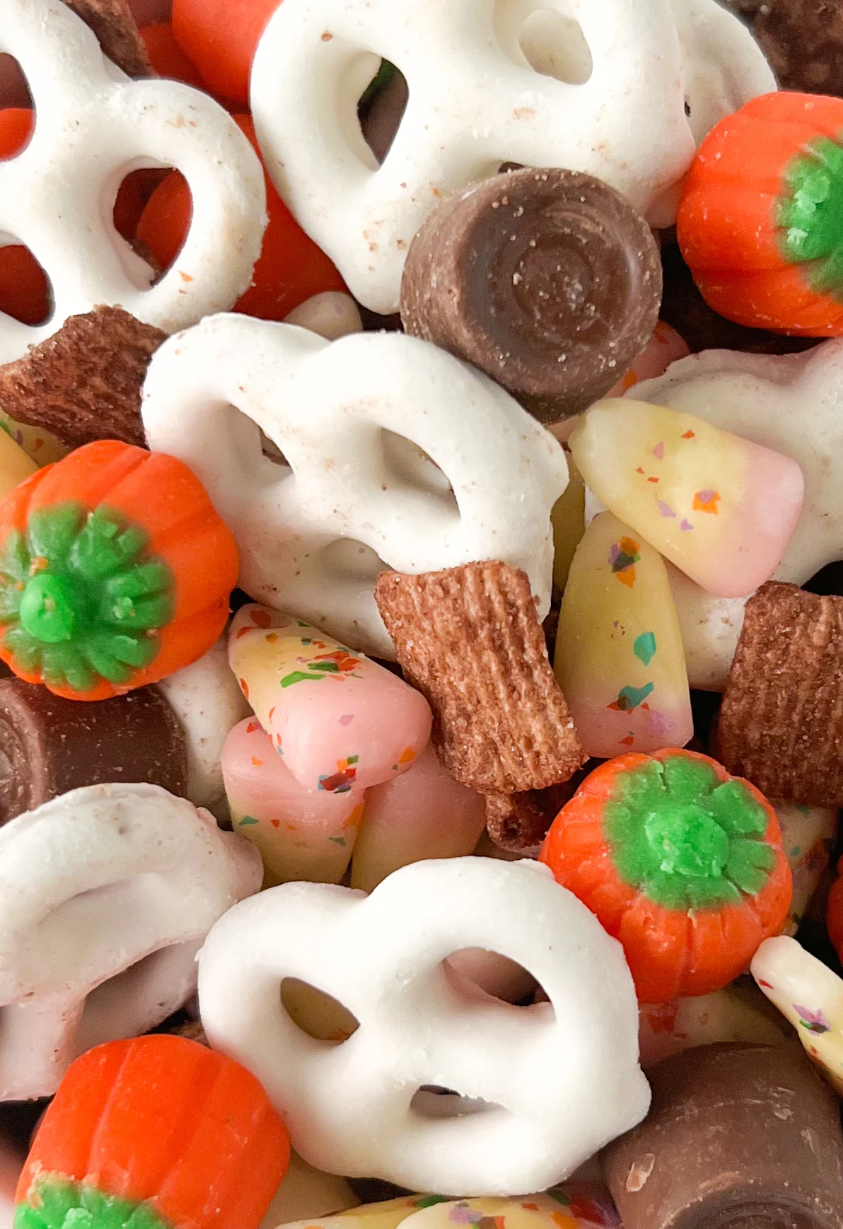 up close view of a fall snack mix with yogurt covered pretzels, pumpkin candies, rolo candies and chocolate cereal.