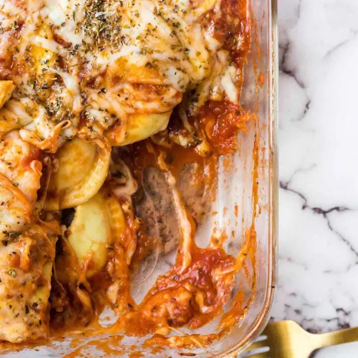 over the top baked ravioli in baking dish with serving removed to reveal sauce, cheese and ravioli