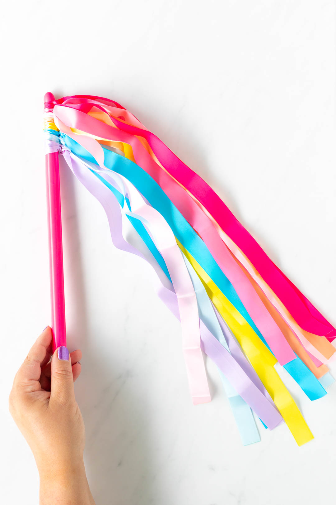 woman holding a dancing wand. a pink drumstick with ribbons in various colors