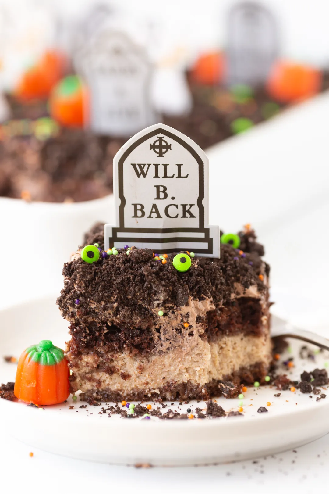 slice of 6 feet under cake on a small plate with pumpkin candy nearby topped with crushed oreo