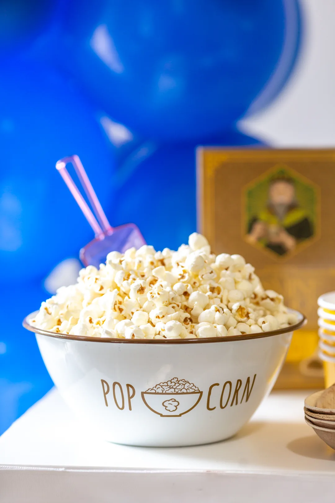 bowl of popcorn on a party table with blue balloons in the background