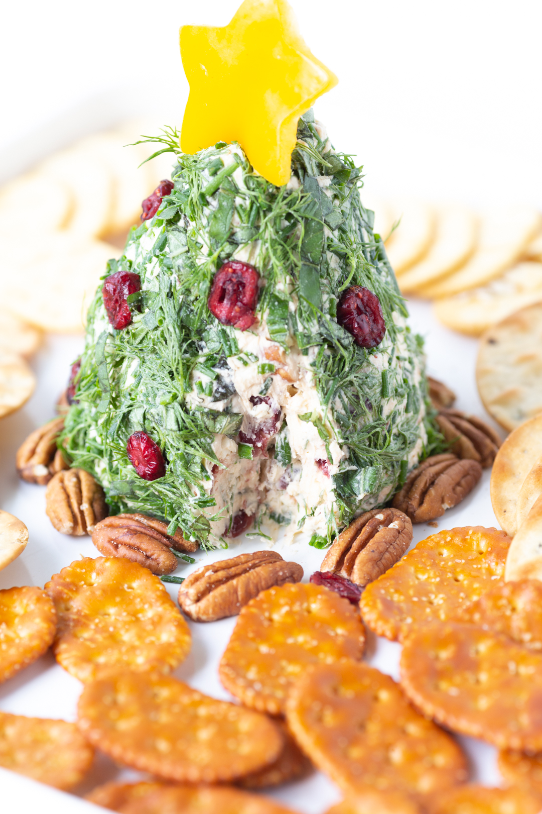 angled down view of christmas tree shaped cheeseball covered with fresh herbs and topped with a yellow pepper star.