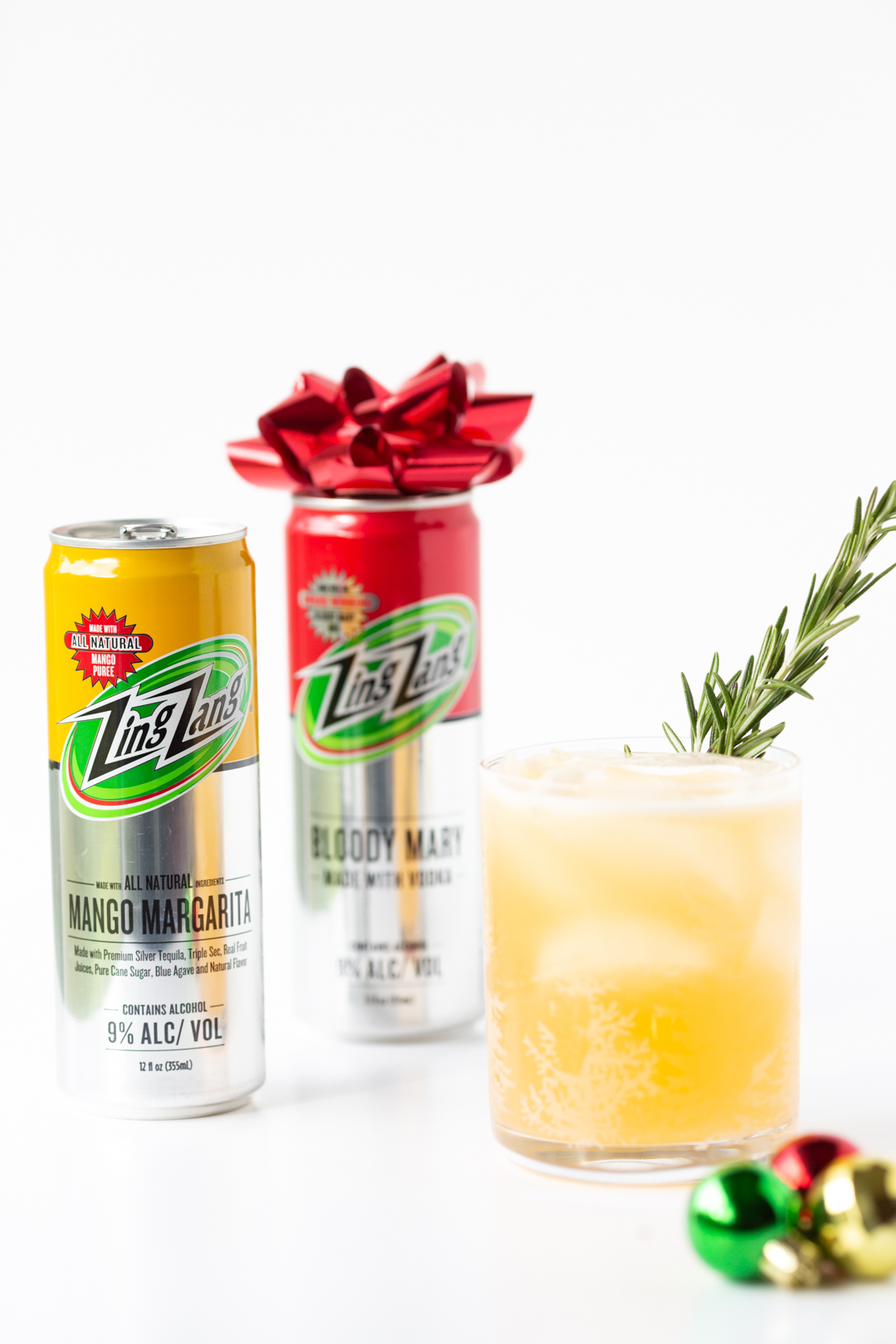 Zing Zang® cocktail cans and mango margarita served in a small festive glass with a spring of fresh rosemary
