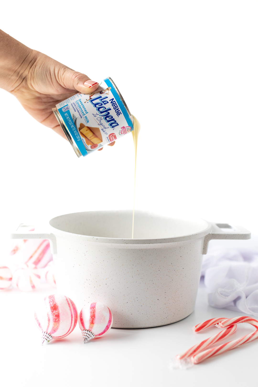 woman pouring can of la lechera sweetened condensed milk into a sauce pan.