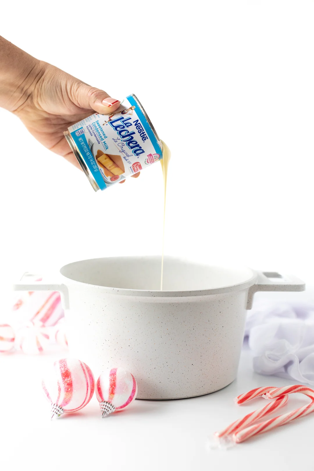 woman pouring can of la lechera sweetened condensed milk into a sauce pan.