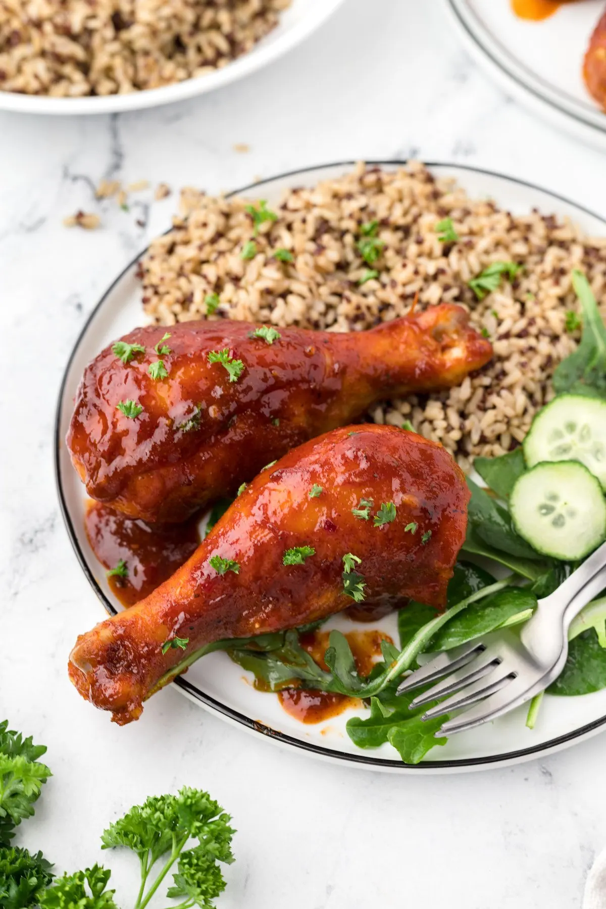 bbq chicken drumsticks served on a dinner plate with wild rice and salad with cucumbers