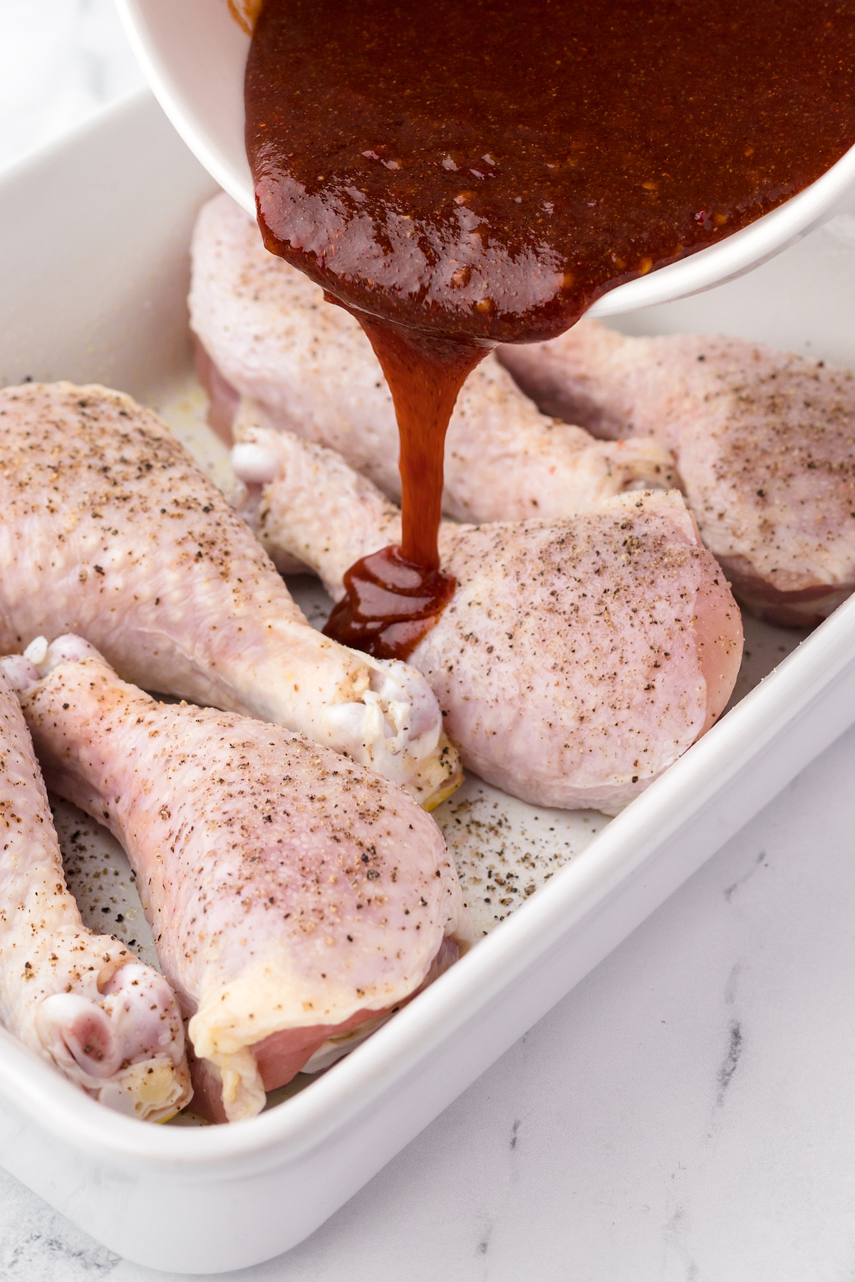 Pouring BBQ Sauce over chicken drumsticks to prepare for baking in oven