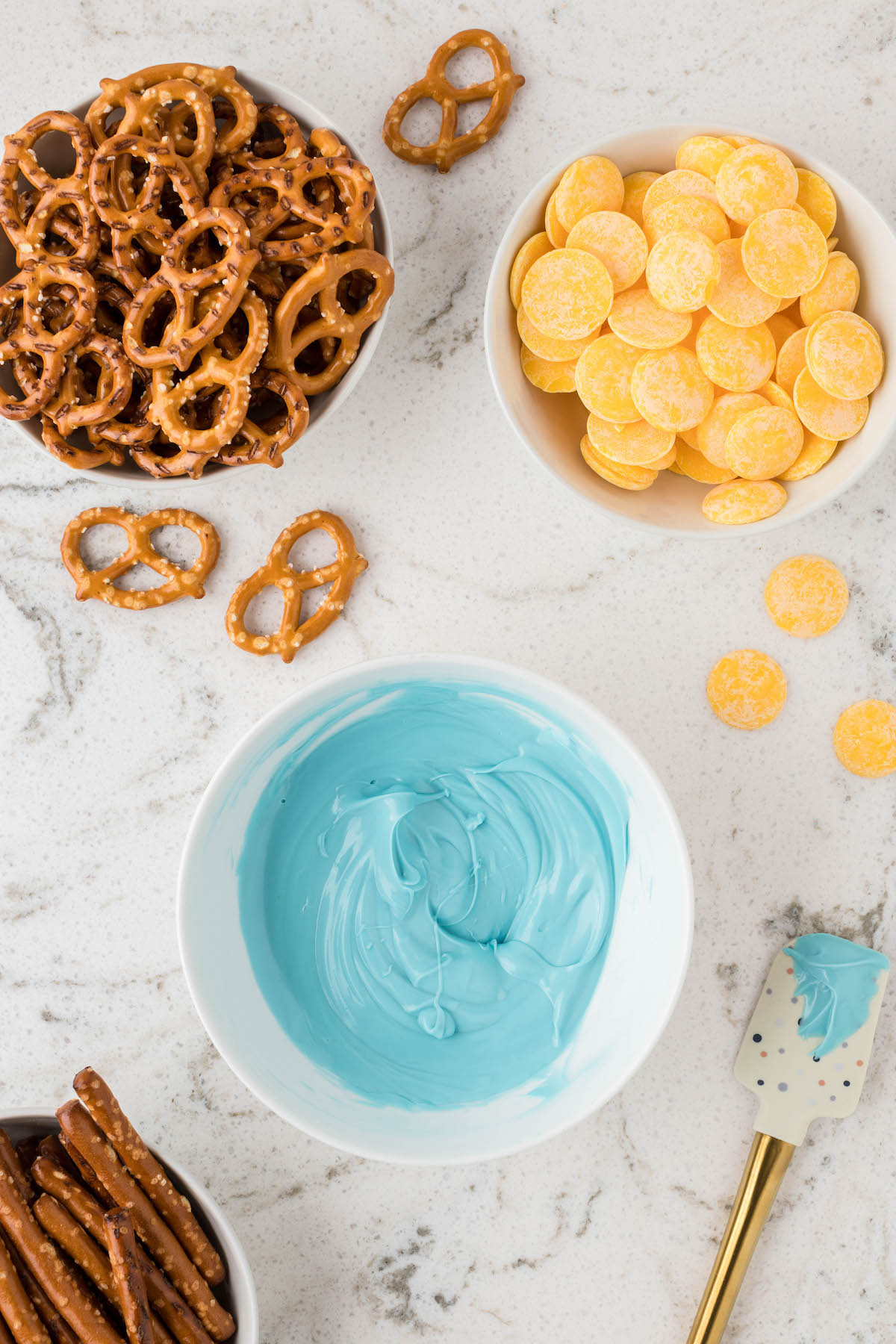 melted blue chocolate, yellow chocolate melts and pretzels set out to prepare butterfly pretzels.
